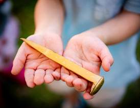 A golden spike from the Red River Railroad Museum Golden Spike Day Celebration held in a child's hands.