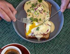 Eggs_Benedict_on_Toast_Being_Cut_Open_Served_with_Coffee_on_a_Patterned_Green_Table