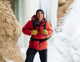Aaron Mulkey in a red jacket and black hat standing in front of a frozen waterfall