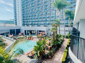 Image of the pool area at the Anaheim Marriott hotel. The photo shows a pool lined with seats and palm trees. The background is the Anaheim Marriott hotel.