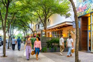 People walking on the sidewalk through the 2ND Street District chatting while holding shopping bags.