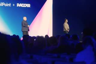 Two executives speaking in front of a room of hundreds of attendees.