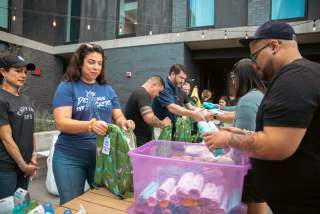 Group of volunteers filling backpacks with care items in an outdoor courtyard.