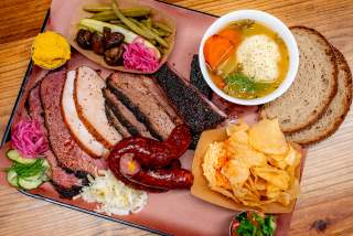 Flat lay image of a tray of smoked meats, side dishes and bread sitting on a tray on a table at Mum Foods.
