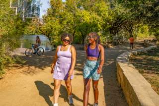 Two women walking along the sunny Hike-and-Bike trail along Lady Bird Lake.