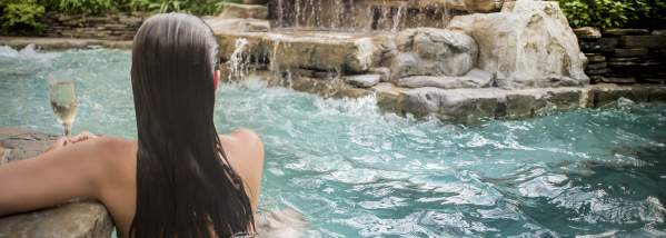 Back-shot of Woman Sipping Wine in Hot Tub with Rock Waterfall