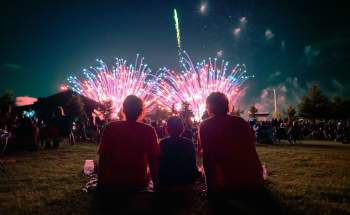 silhouettes of three people (a family) sitting with fireworks going off in front of them.