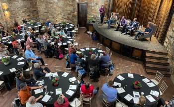 Small meeting at The Sanctuary, speakers on stage, audience at round tables