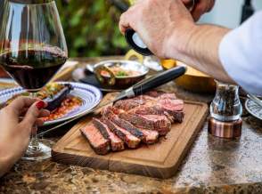 Seasoning medium rare steak with salt grinder, cut on wooden board on a restaurant table.