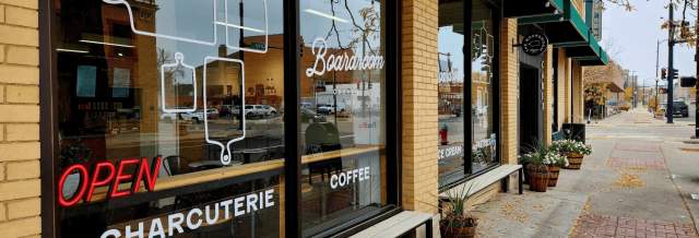 A storefront with a sign that reads "open" and the words "The Boardroom" above it. Snow is on the ground and there is a snowy tree in the background.