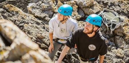 young couple with climbing equipment looking up at cliff wall