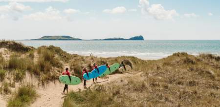 Surfers walking along dunes with their surfboards towards the beach