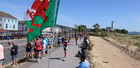 crowd cheering on competitors running along the swansea beach front during the Ironman Swansea event