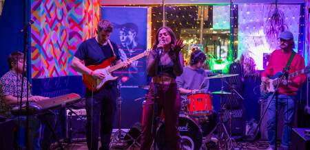 A young five piece band with female singer playing on a colourful stage.