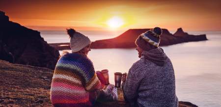 a couple share coffee while the sun sets against worms head