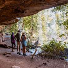 A tour guide stands with two tour guests looking out at a waterfall