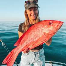 A woman in a boat holding a freshly caught Red Emporer