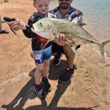 A child holding a Trevally, freshly caught from the shore at Port Hedland. A man crouches behind the child, supporting him