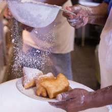 Dusting powdered sugar on a fresh pile of beignets