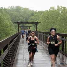 runners racing across a greenway bridge in the rain
