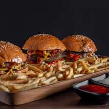 three burgers on a plate with fries and sauces