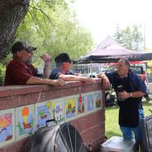 Three men, smiling and talking. Two are leaning against the wall.