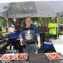A man smiling with three trays of smoked bbq ribs.