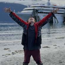 Boy celebrating the sunshine arms raised, cruise ship docked in backdrop