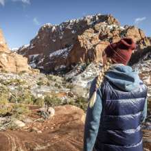 Woman dressed for colder weather hiking into red rock formations in Kolob Canyons, the North Side of Zion National Park.