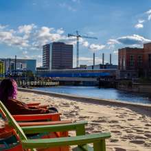 A person sitting in the chairs on the beach at Rotary Park, enjoying the view of Downtown Lansing