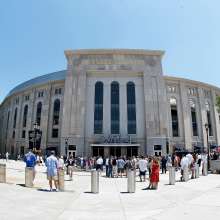 Daytime straight-on view of a Yankees Stadium entrance with a plaza full of fans