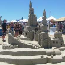 People standing around a sandcastle at Texas SandFest, showcasing impressive sand art and sculptures