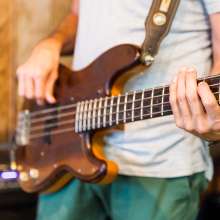 A close up of a guy strumming a brown guitar.