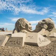 Sand sculpture of child holding mans mouth in a smile.