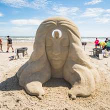 Sand sculpture of a women wiht a hole in the middle of ther head showing a smaller version of her.