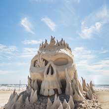 Skull sand sculpture with flames coming through it.
