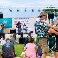 A couple dances in front of a stage where a band is performing. A crowd sits in the grass.