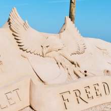 Sand sculpture that says "let freedom reign" with an eagle behind it.