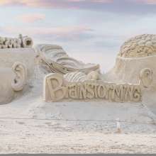 Sand sculptures of two heads with the brain exposed with a torndado in the middle.