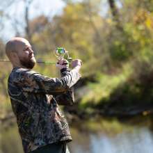 A bearded man wearing camouflage holds a fishing rod.
