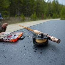 fly fishing line and tackle on a flat surface set in front of a fisherman tying a line