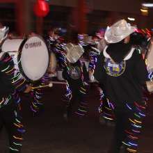 Gadsden's Marching Band Drumline marching down the parade with hats and uniforms strung up with Christmas lights.