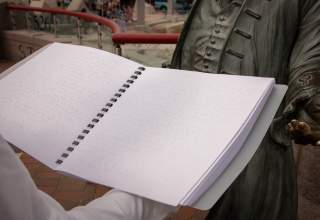 A woman holds the City of Presidents braille booklet in front of a bronze statue in Downtown Rapid City.