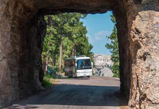 tour bus passing through the tunnel of iron mountain road with mount rushmore in the background