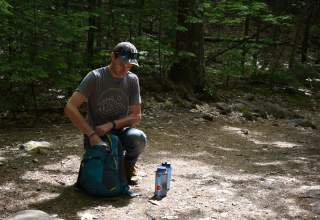 Man packing backpack with water bottles next to him on hiking trail in the Black Hills