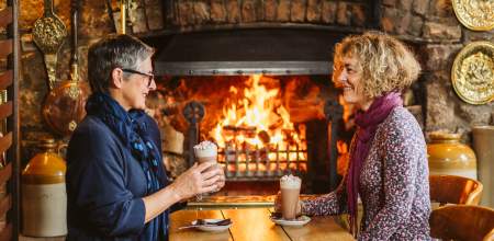 two women enjoying hot chocolate in a cafe near a fireplace