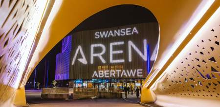 View of the main entrance of swansea arena from the bridge lit up at night