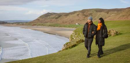 Couple walking along rhossili bay coastline