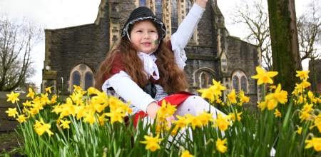 A young girl in traditional welsh costume sits in a patch of daffodils