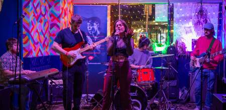 A young five piece band with female singer playing on a colourful stage.